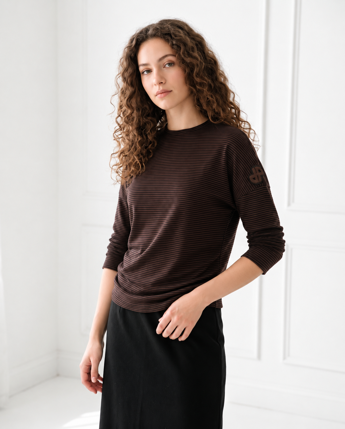 Brown long-sleeve top with a drop shoulder, fine horizontal stripes, and a sleeve logo