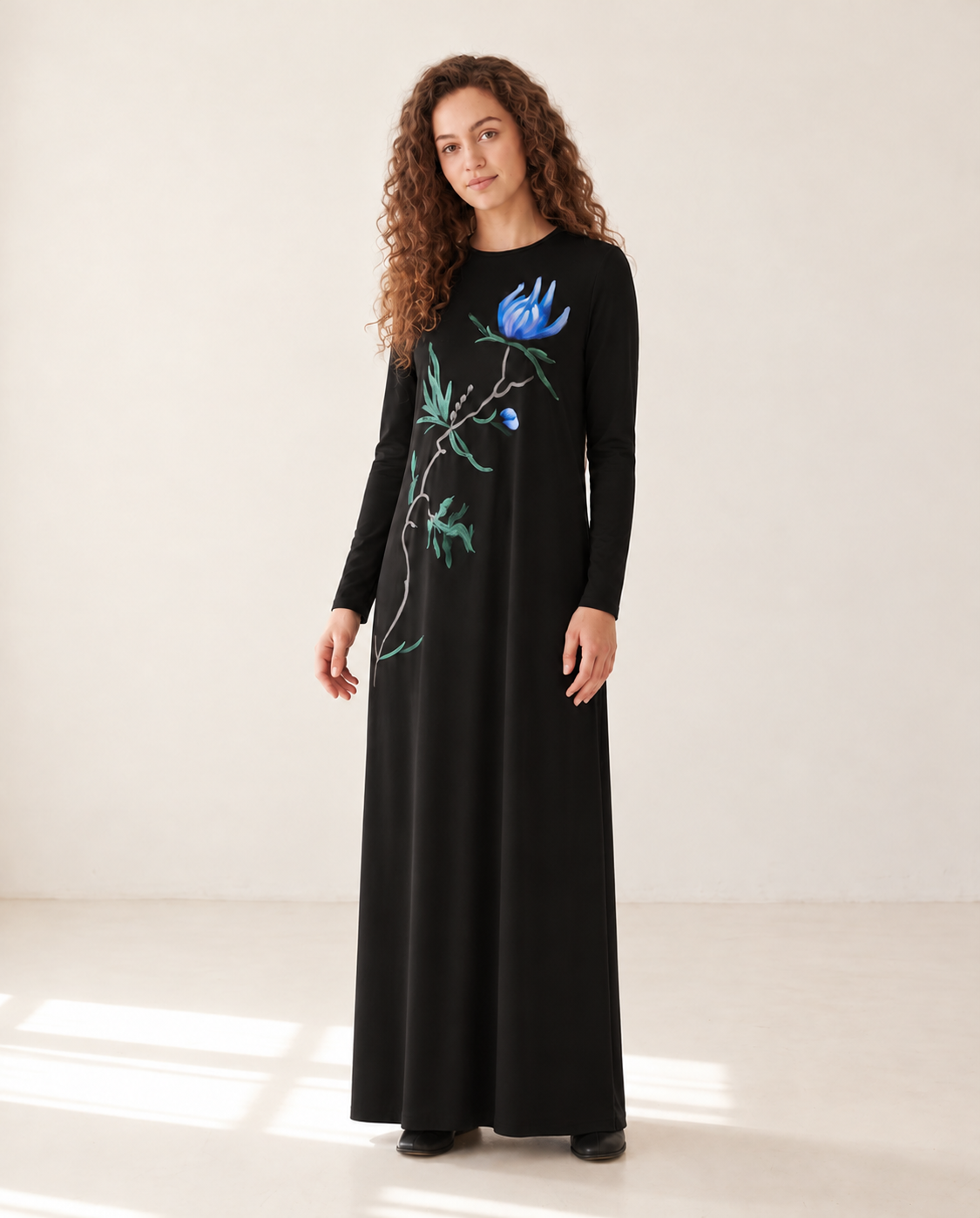 Model wearing a black long-sleeve nursing nightgown with a blue floral print and floor-length skirt.